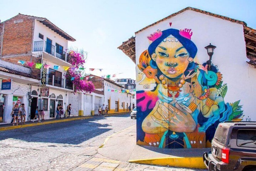 Una calle con un mural de una figura colorida, edificios y peatones. 1
