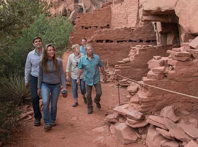 A group of people walking on a dirt path beside ancient ruins. 4