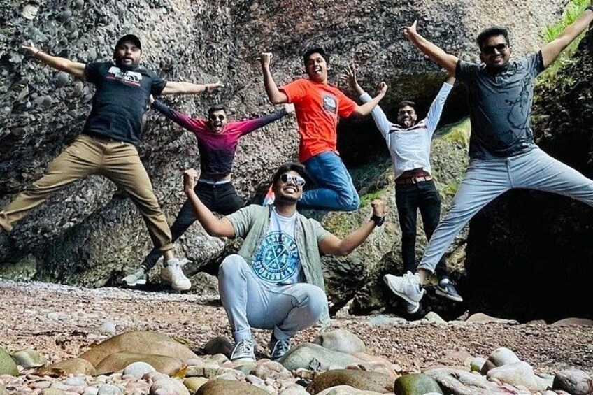 A group of people posing energetically on a rocky terrain with a cliff in the background. 1