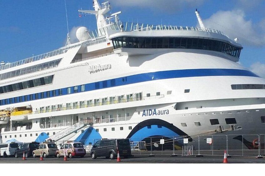 A large white cruise ship with blue accents and the name 'AIDAura' on its side. 3