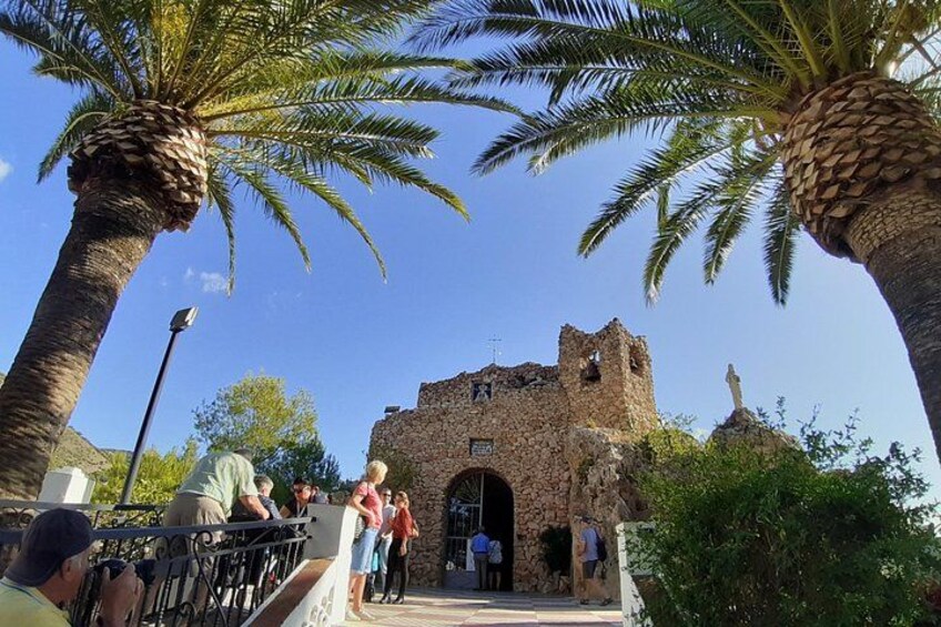 Un edificio de piedra histórico con una torre, palmeras y gente en una plataforma de observación. 1