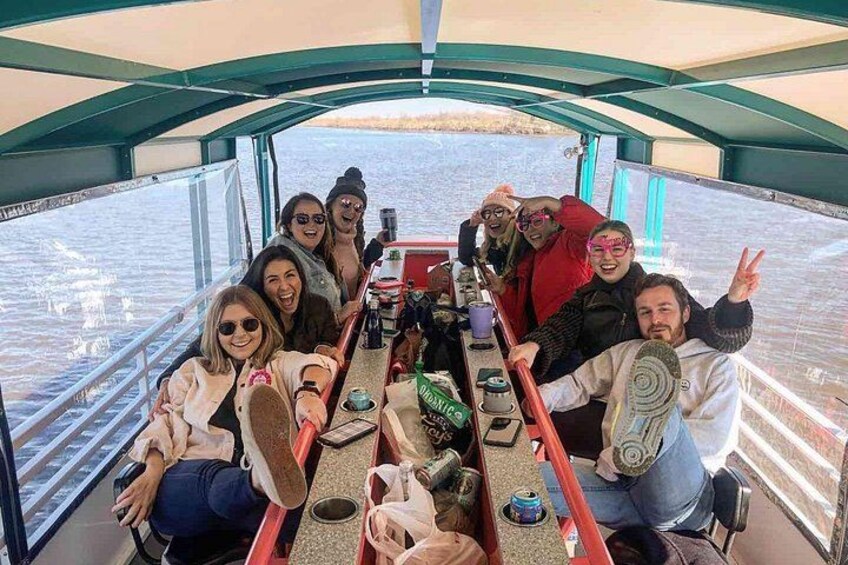 A group of people on a boat with a table in the center, surrounded by water. 1