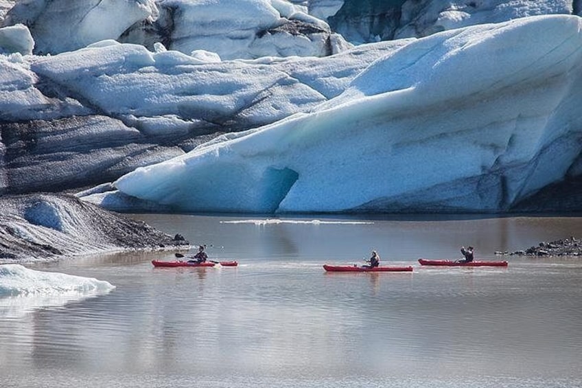 Kayakers in red kayaks on a calm body of water surrounded by large ice formations. 4