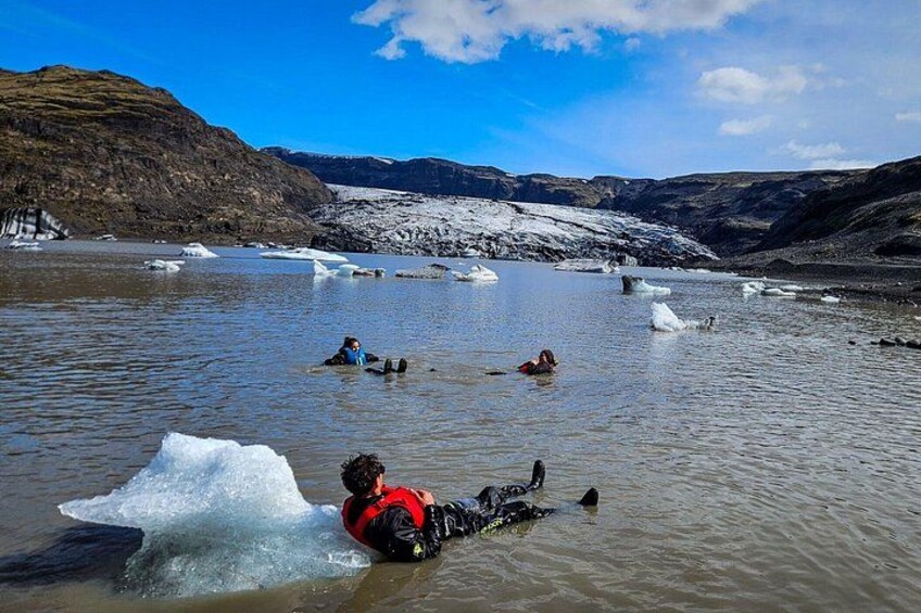 Una persona con chaqueta roja flotando sobre un glaciar, con icebergs en un paisaje montañoso y frío. 2