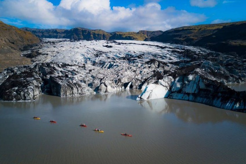 Un glaciar con un lago parcialmente congelado, rodeado de montañas. Hay kayaks en el agua. 3