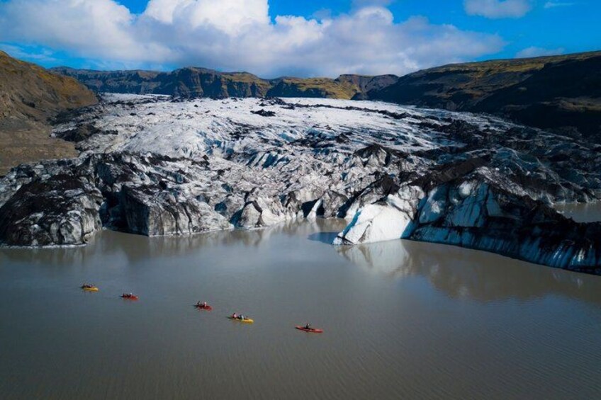 Un glaciar con un lago parcialmente congelado, rodeado de montañas. Hay kayaks en el agua. 2