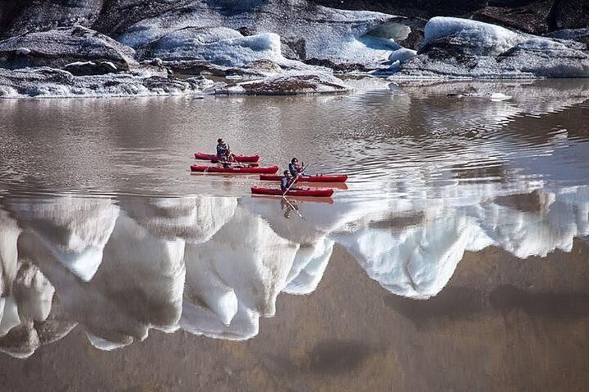 Two people kayaking on a calm river with ice formations in the background. 3