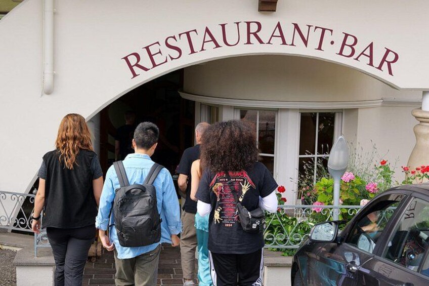 Un bar restaurante con gente entrando y un coche estacionado afuera. 4