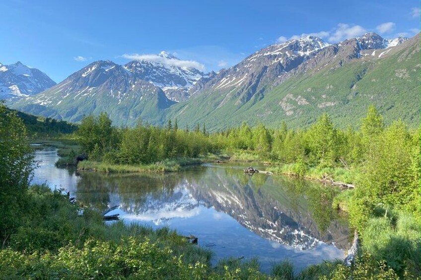 A mountain lake with reflections, surrounded by greenery and snow-capped peaks. 1