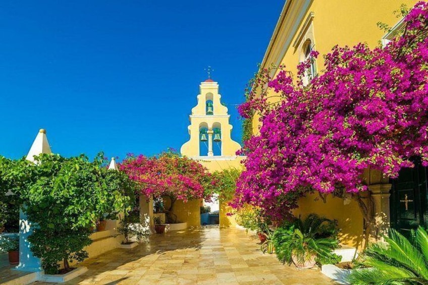 Ein Innenhof mit einem gelben Gebäude, einem Glockenturm und Bougainvillea-Blumen. 5