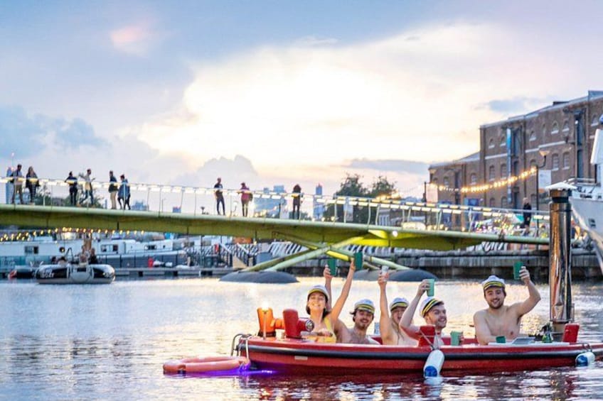 A group of people on a red boat in a river, with a bridge and buildings in the background. 2