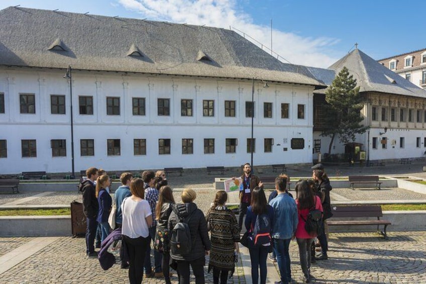 Een groep mensen staat voor een wit gebouw met een pannendak. 1