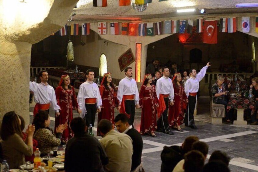 Un gruppo di persone in abiti tradizionali si esibisce su un palco, con delle bandiere sullo sfondo. 3