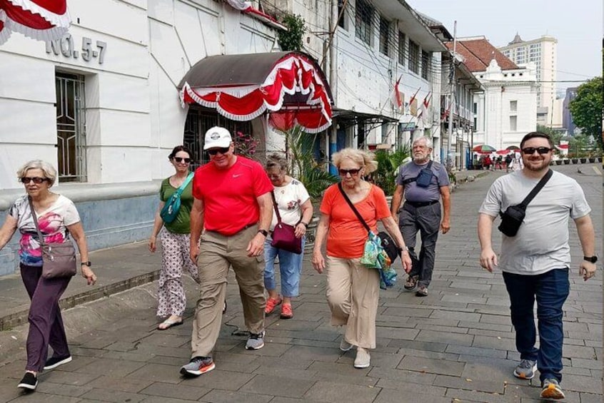 A group of people walking on a paved street with buildings and flags in the background. 4