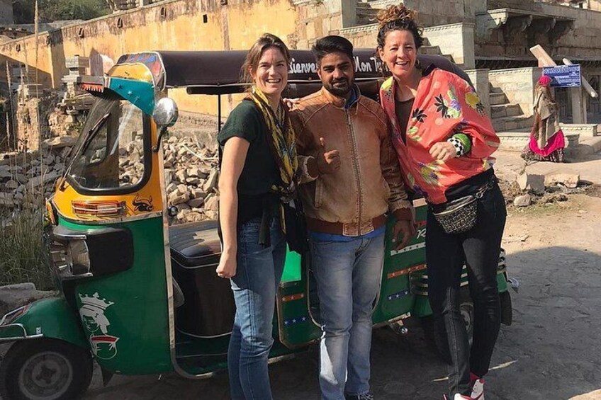 Tres personas de pie frente a un auto-rickshaw verde, con un sitio de construcción al fondo. 5