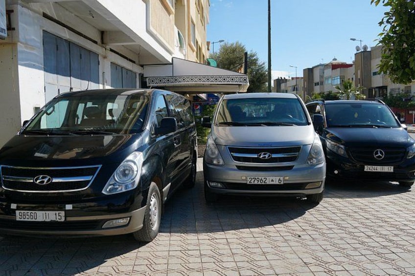 Three cars parked on a paved street, a building with a white facade, and a clear blue sky. 3