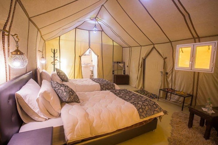 A tent with two beds, a table, and a hanging light fixture. 2