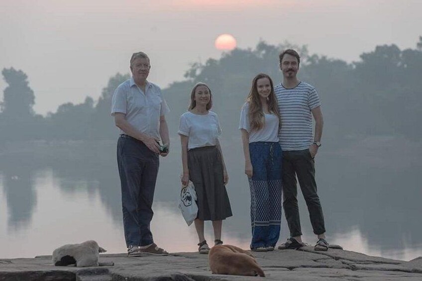 A group of people standing on a dock by a calm body of water during sunrise or sunset. 3