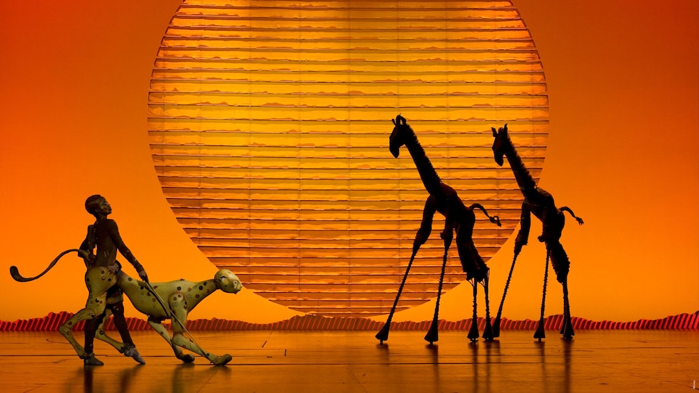Un palco con un grande sfondo giallo, una giraffa, un leone e una figura umana. 1