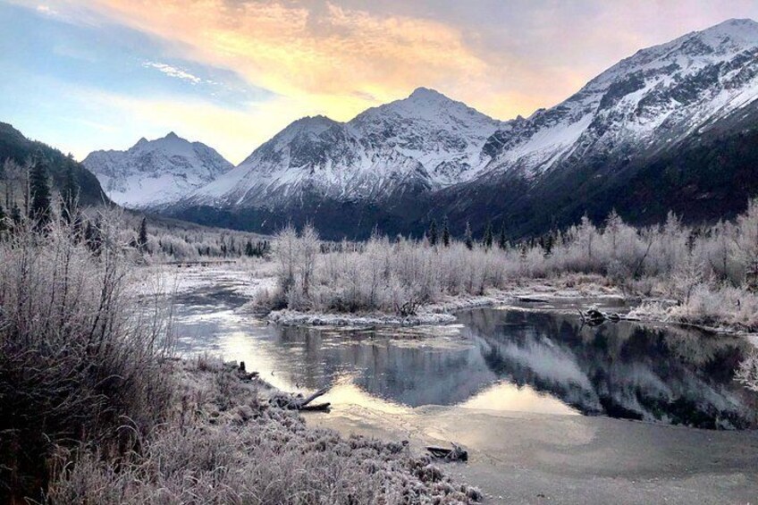 A snow-covered mountain range, a river reflecting the sky, and a forested valley. 1
