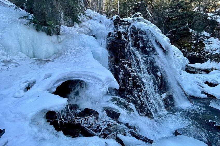 A frozen waterfall with snow-covered rocks and trees in the background. 3