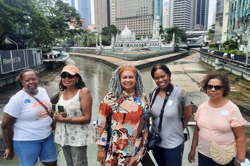 A group of people standing by a river with a cityscape in the background. 1