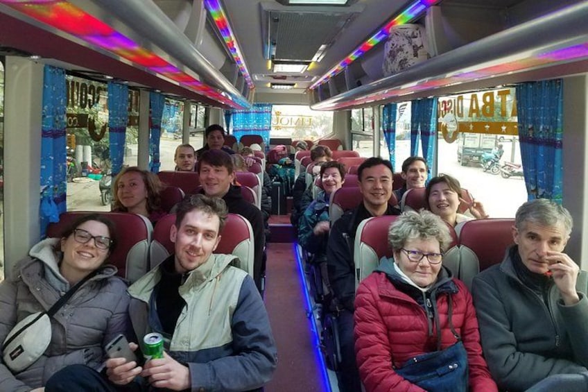 A bus interior with passengers seated, windows with curtains, and a sign on the wall. 3