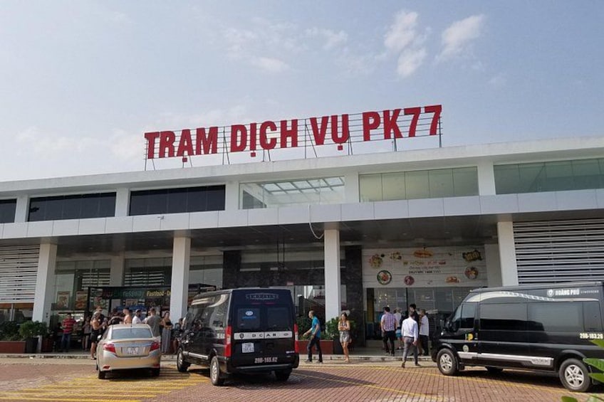 A building with a sign reading 'TRAM DICH VU PK77' and several people walking in front. 5