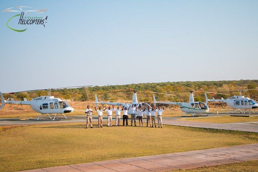 A group of people standing in front of three helicopters on a grassy field. 2
