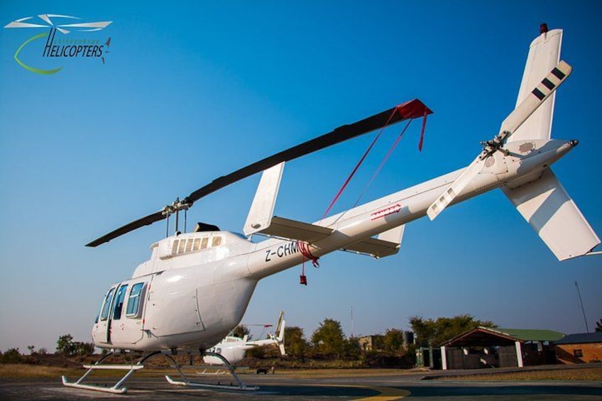 Un helicóptero blanco con la matrícula Z-CHIM sobre una plataforma de tarmac, con un cielo azul despejado al fondo. 3