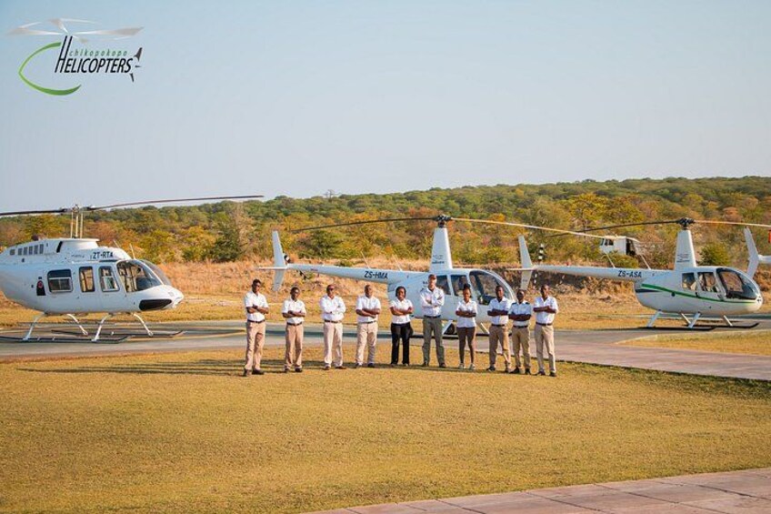 Un grupo de personas de pie frente a un helicóptero en un campo cubierto de hierba, con árboles al fondo. 4