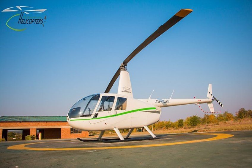 Un helicóptero blanco con franjas verdes estacionado en una plataforma de tarmac con un edificio al fondo. 2