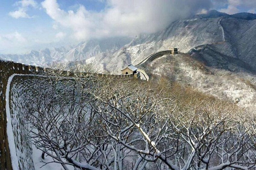 A snow-covered landscape with a bridge, bare trees, and mountains in the background. 5