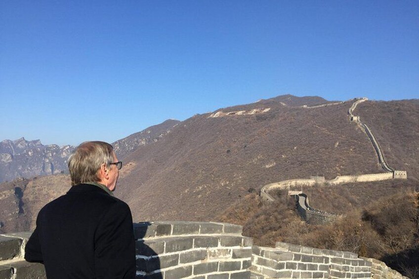 A person standing on a wall overlooking a mountainous landscape with a winding road. 4
