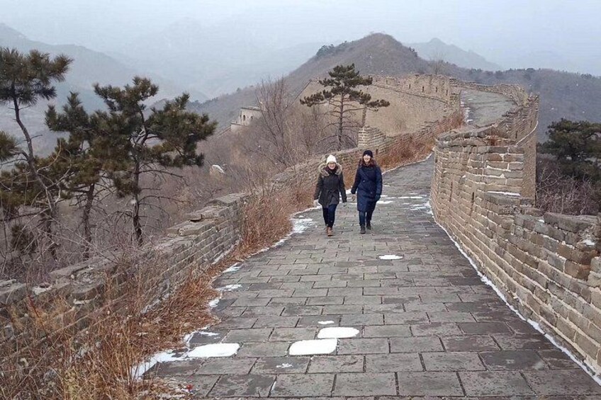 A pathway along the Great Wall of China with snow patches and sparse vegetation. 3