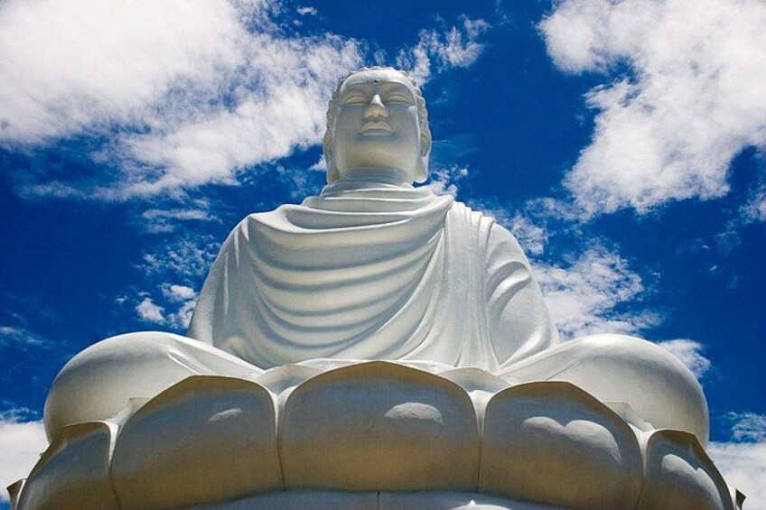 Une grande statue blanche représentant une figure assise, se détachant sur un ciel bleu parsemé de nuages. 1
