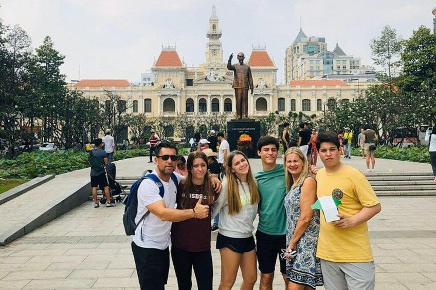 A group of people posing in front of a historical building with a statue. 1