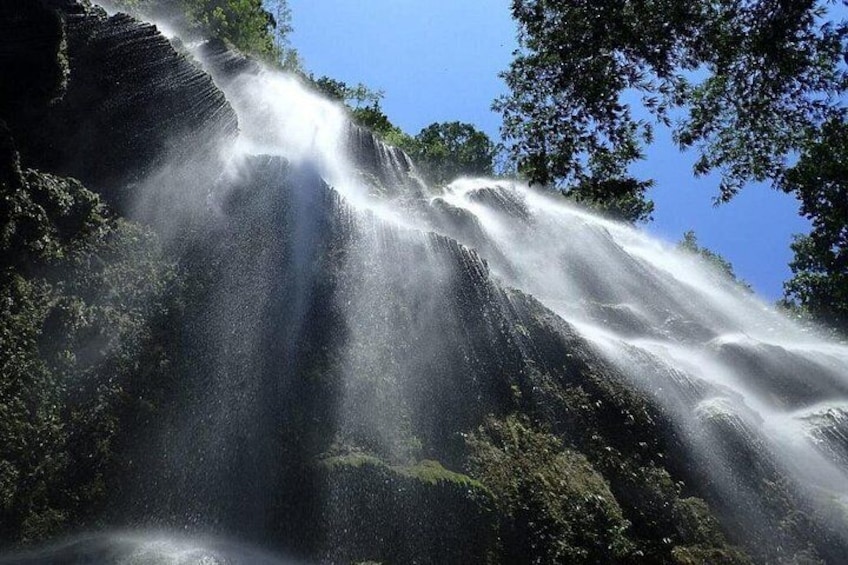 Une cascade se déversant sur une falaise rocheuse, le tout étant entouré d’une végétation luxuriante. 1