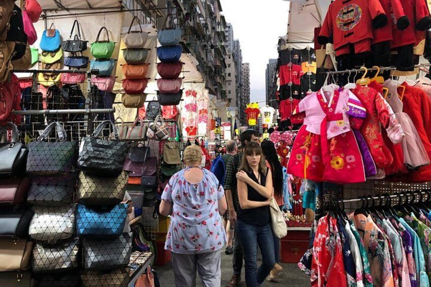 A market with various stalls selling handbags and traditional clothing. 1