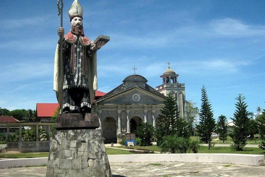 A statue of a religious figure, a church with a bell tower, and a clear sky. 3