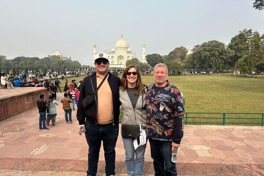 Three people standing in front of the Taj Mahal with a crowd in the background. 4