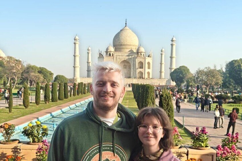A person standing in front of the Taj Mahal with a garden and visitors in the background. 5