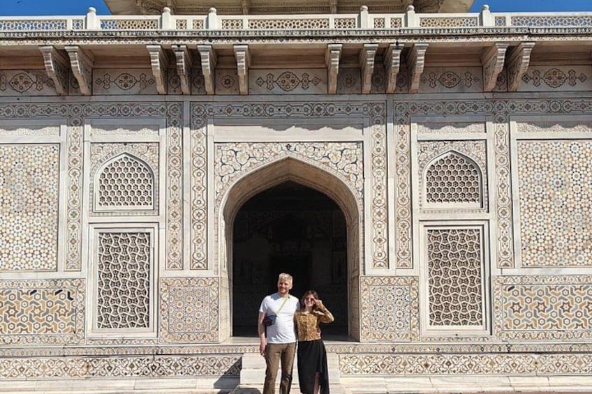 A man and a woman standing in front of a detailed architectural structure with intricate patterns and an arched doorway. 4
