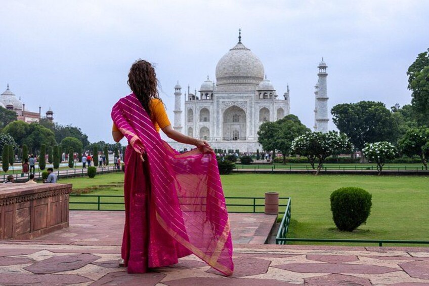 A person in a pink saree standing in front of the Taj Mahal. 4