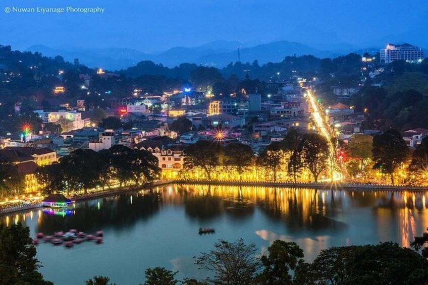 A cityscape at dusk with illuminated buildings, a river, and a bridge. 1