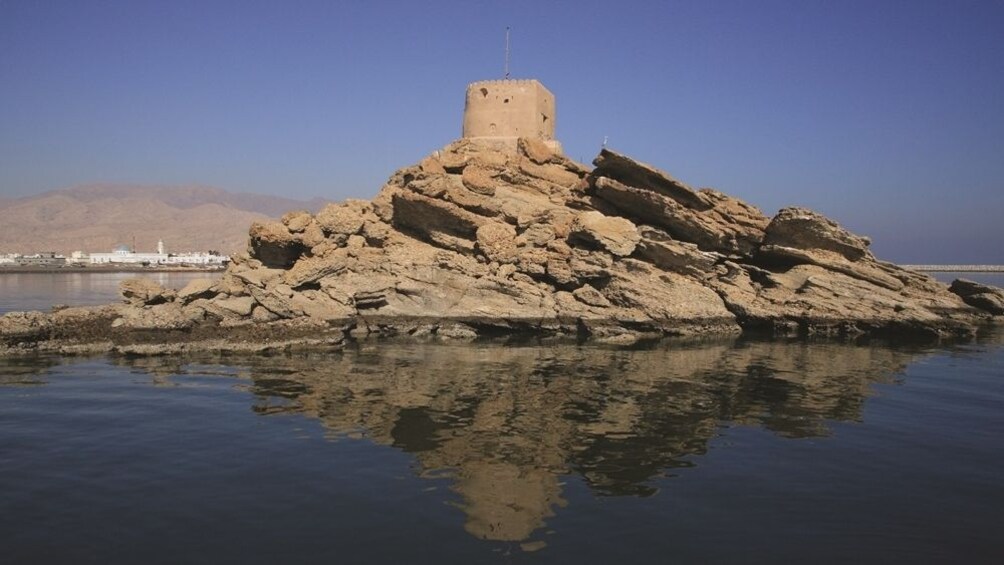 Una isla rocosa con una torre en el centro, rodeada de aguas tranquilas y un cielo despejado. 5