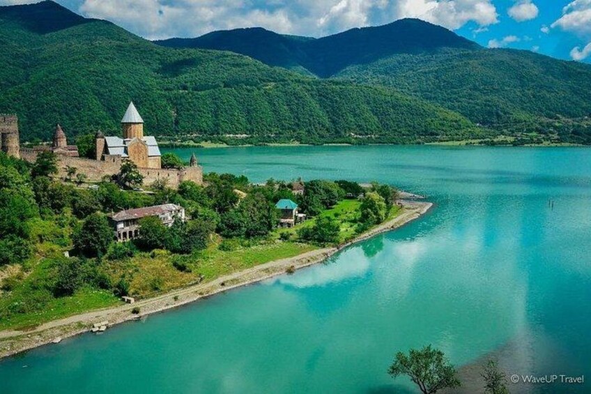 Un castillo histórico junto a un lago, rodeado de exuberante vegetación y montañas. 2