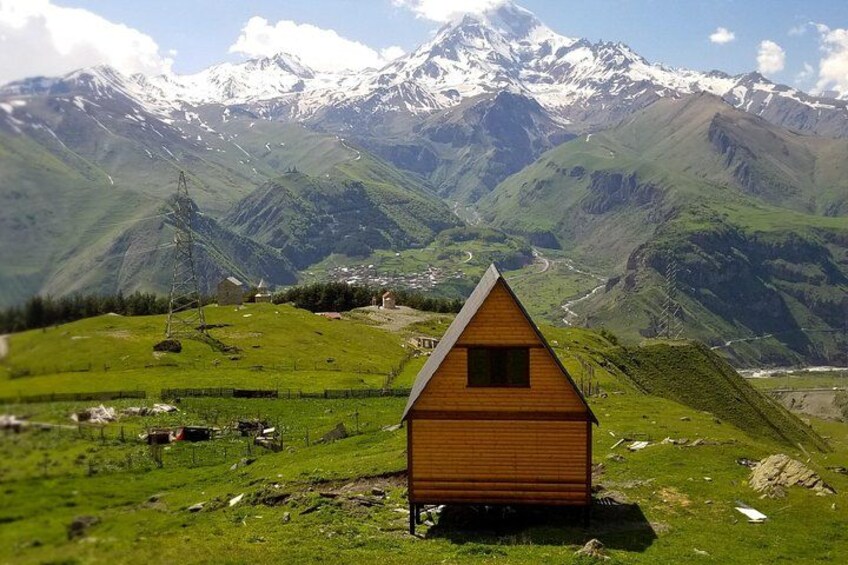 Una cabaña de madera en una colina cubierta de hierba, con una cordillera en el fondo. 5