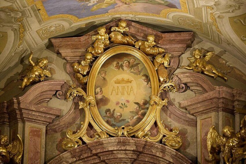An ornate ceiling with a central oval frame, golden cherubs, and the name 'ANNA'. 5