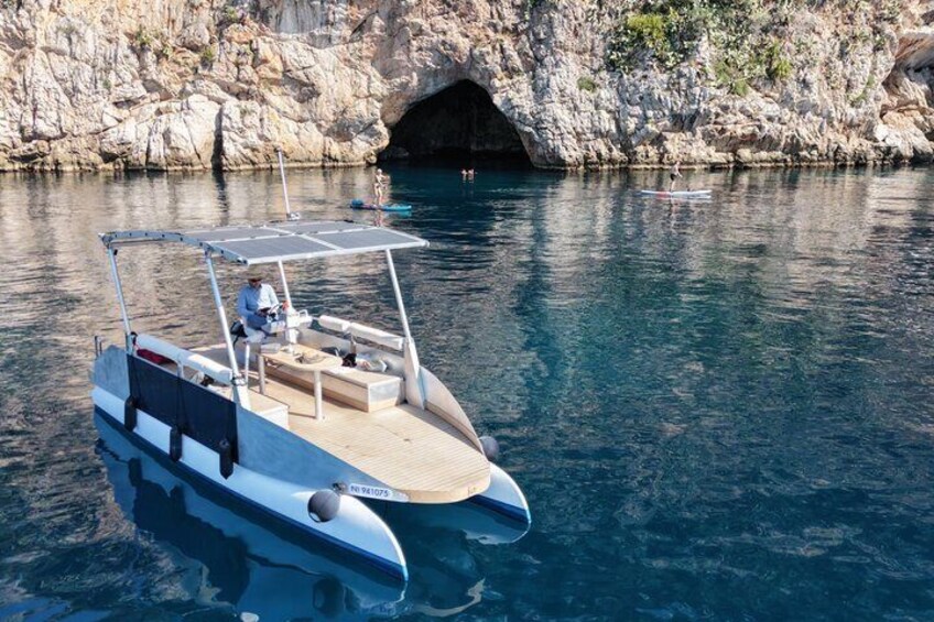 A small boat with a canopy, docked near a rocky coastline with a cave entrance. 1